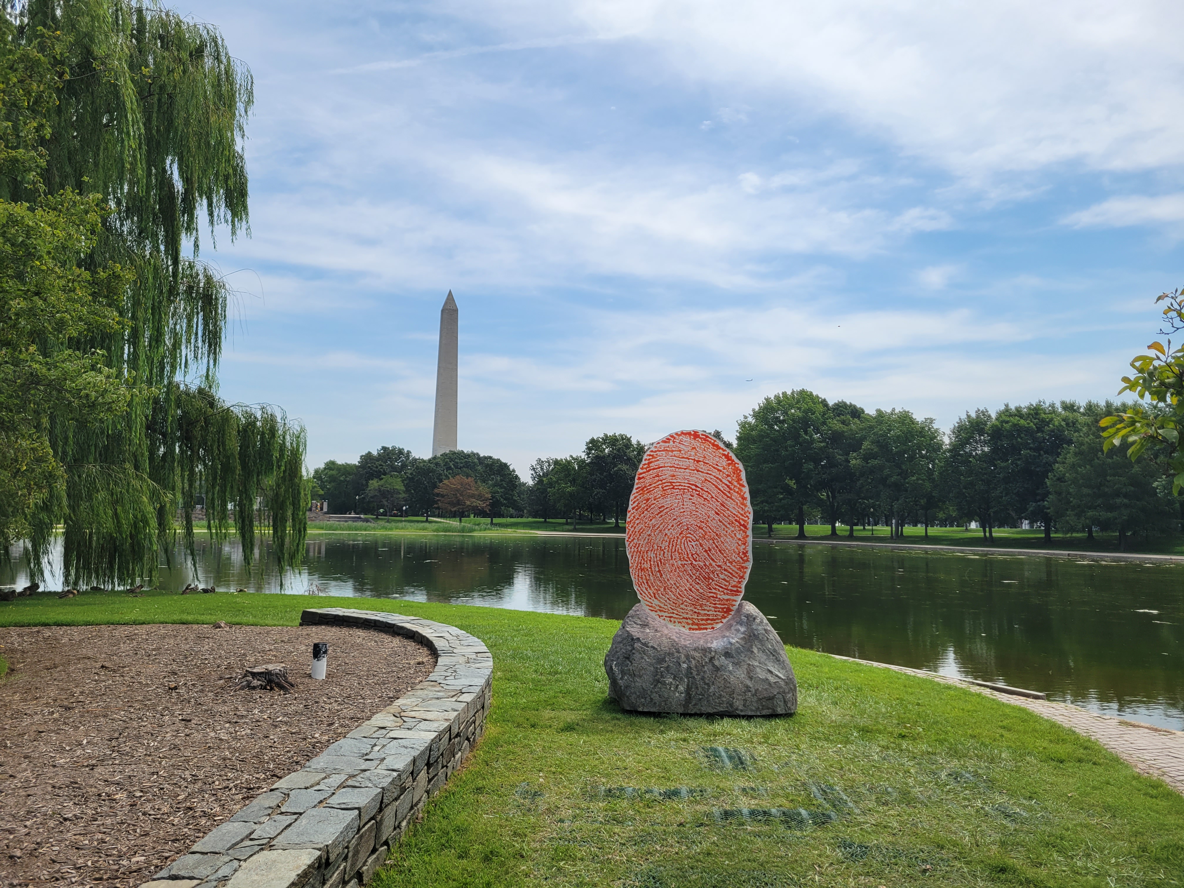 A view of a giant red and white fingerprint in the foreground and the Washington Monument in the background.