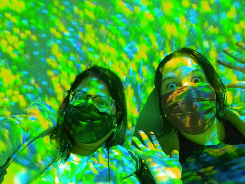 Two women sitting washed in green and blue light.